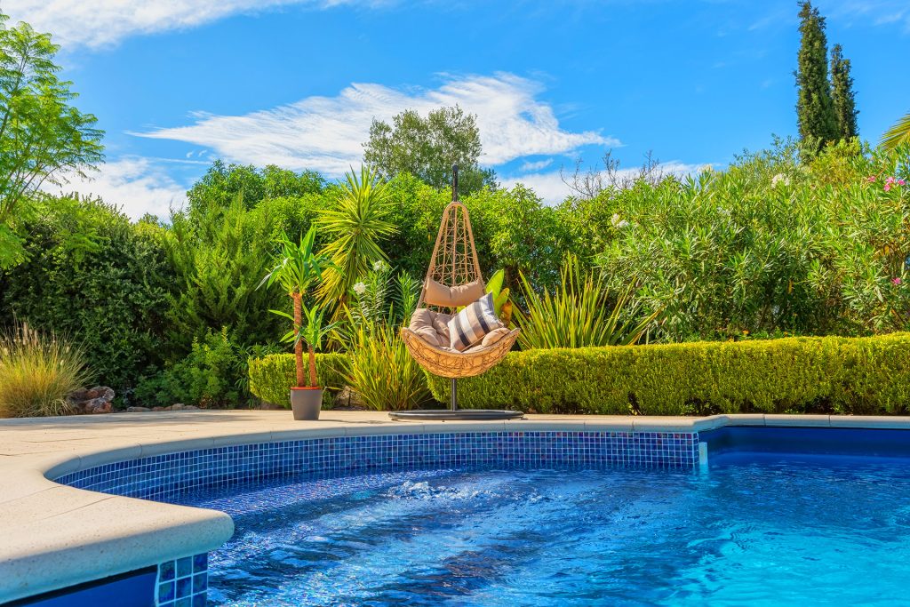Backyard swimming pool with hanging egg chair and lush landscaping